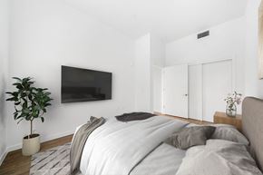 Sacramento apartment for rent - A bedroom with a bed, a plant, and a television mounted on the wall.