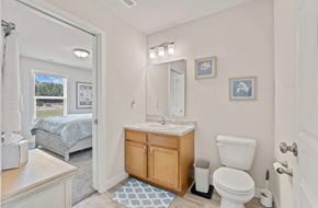 Fort Wayne apartment for rent - A bathroom with a white toilet, sink, and a bedroom with a window in the background.