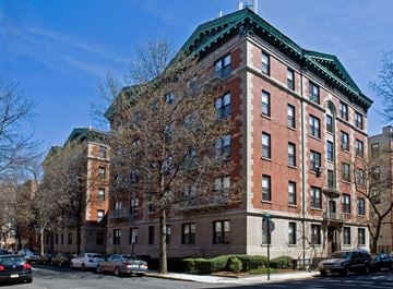 Hoboken apartment for rent - A red brick building with a green roof sits on a street corner.
