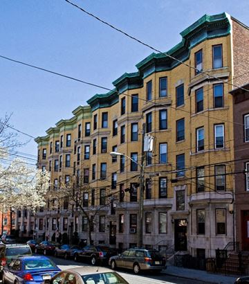 Hoboken apartment for rent - A row of brown and green buildings with cars parked in front.