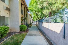 Rialto multi-family for rent - A sidewalk runs between two buildings with a metal fence on one side.