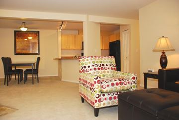 Renton apartment for rent - A living room with a black chair, a black ottoman, a black table, a black refrigerator, a black cabinet, a black lamp, a painting, a dining table, and a dining table with chairs.
