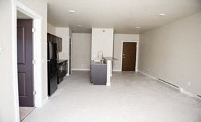 Fargo apartment for rent - an empty living room with a kitchen and a black refrigerator