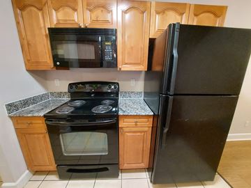 Marble Falls apartment for rent - A black refrigerator stands next to a black microwave and oven in a kitchen.