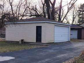 Gary house for rent - A small garage with a black door is surrounded by a driveway and trees.