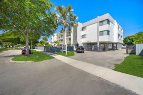 North Miami apartment for rent - a large white building with palm trees and cars parked in front of it