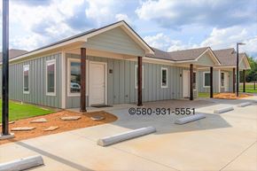Durant apartment for rent - A small building with a grey and white exterior is surrounded by a concrete walkway.