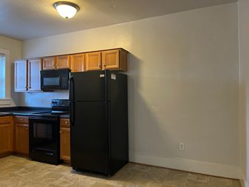 Roanoke apartment for rent - A black refrigerator stands in a kitchen with wooden cabinets.