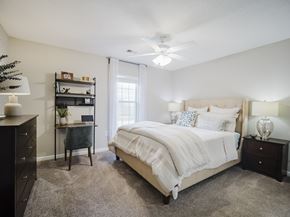 Newnan apartment for rent - A bedroom with a large bed, a desk, and a ceiling fan.