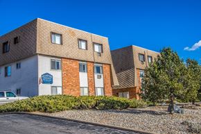 Arvada apartment for rent - two brick and white buildings with a tree in front of a parking lot