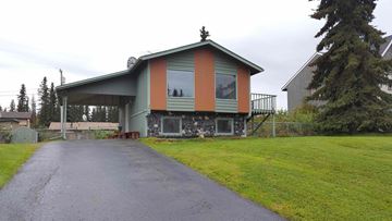 Soldotna house for rent - A house with a green and orange exterior sits on a grassy area with a driveway leading to the front door.