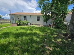 Bay City house for rent - A small house with a brown roof and a white exterior is surrounded by a grassy area and trees.