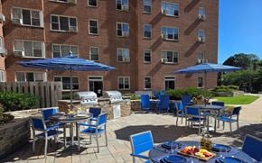 Baltimore apartment for rent - A patio with blue chairs and umbrellas is set up outside a brick building.