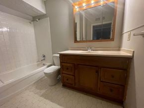 Louisville apartment for rent - A white tiled bathroom with a wooden vanity and a white toilet.