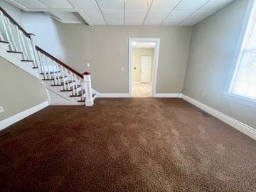 Louisville house for rent - a carpeted living room with stairs and a door to a hallway