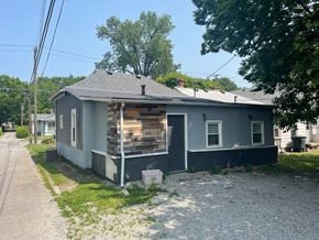Jeffersonville house for rent - A house with a grey and white exterior is surrounded by a gravel area and a grassy patch.