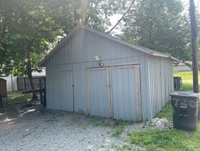 Jeffersonville house for rent - A grey metal shed with a door and a window is surrounded by trees.
