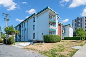 North Vancouver apartment for rent - A white building with a green roof is surrounded by a grassy area and a sidewalk.
