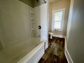 Louisville house for rent - A white bathtub with a shower head and a toilet in a bathroom with wood flooring.