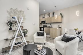 Rochester Hills apartment for rent - A modern living room with a white chair, a black coffee table, and a white shelf with a plant on it.