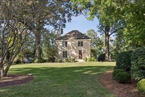 Newport News house for rent - A house with a brown roof and white walls is surrounded by green trees and bushes.