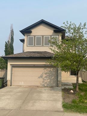 Edmonton house for rent - a tan house with a garage door and a tree