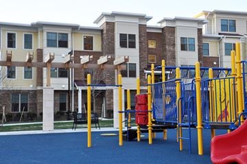 Jersey City apartment for rent - A playground with a blue surface and yellow and red play equipment in front of apartment buildings.