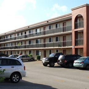 Mangilao apartment for rent - A parking lot with cars and a building in the background.