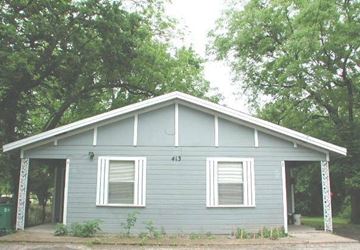 Mckinney apartment for rent - A small house with a grey siding and a white window is surrounded by trees.