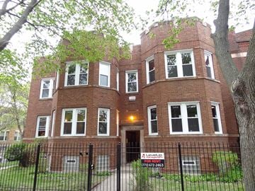 Chicago apartment for rent - a large brick building with a yard and a fence in front of it