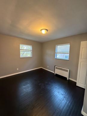 Cincinnati apartment for rent - A room with a white ceiling, a window with blinds, a white radiator, and a wooden floor.