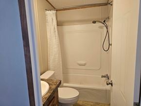 Shawnee house for rent - A white toilet sits next to a white bathtub in a small bathroom.