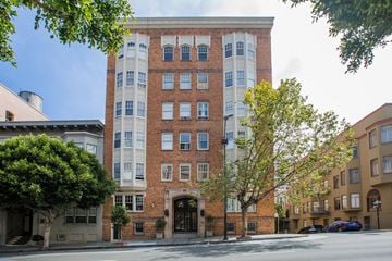San Francisco apartment for rent - A tall building with a mix of red and white bricks stands between two trees.