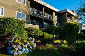 New Westminster apartment for rent - A building with a balcony and a garden in front.