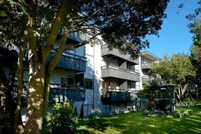 Victoria apartment for rent - A white building with balconies is surrounded by trees and grass.