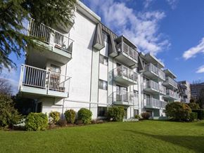 Victoria apartment for rent - A white apartment building with balconies and green bushes in front.