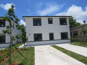 Miami apartment for rent - the back of a white building with a sidewalk and grass