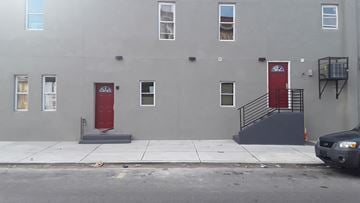 Philadelphia apartment for rent - A grey building with a red door and a black car parked in front.
