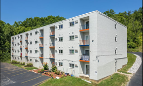 Cincinnati apartment for rent - A white apartment building with orange railings and a parking lot in front.