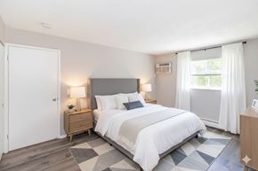 Cincinnati apartment for rent - A bedroom with a large bed, a nightstand with a lamp, and a window with curtains.