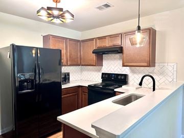 Greenville house for rent - A black refrigerator is in a kitchen with brown cabinets and a black stove.