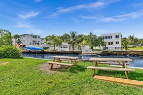 Miami apartment for rent - A serene lawn with two wooden benches overlooks a calm body of water with two buildings in the background.