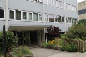 Vancouver apartment for rent - A grey building with a small garden in front.