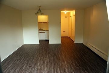 Vancouver apartment for rent - A room with wooden floors and a kitchen in the background.
