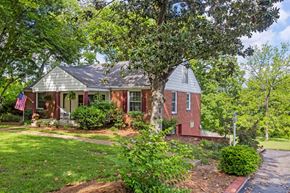 Nashville apartment for rent - A house with a flag on the porch is surrounded by greenery.