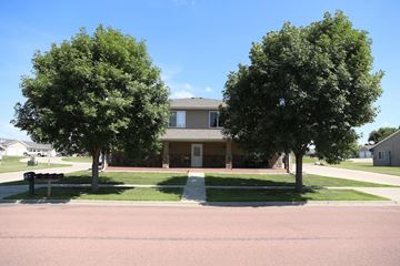 Dell Rapids apartment for rent - A building is surrounded by two trees and a grassy area.