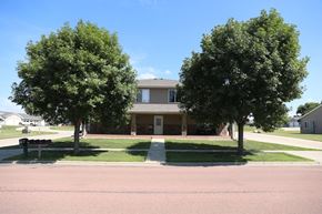 Dell Rapids apartment for rent - A building is surrounded by two trees and a grassy area.