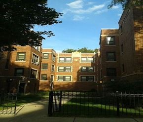 Chicago apartment for rent - a view of a group of brick buildings from behind a gate