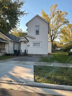 Lima house for rent - A house with a white siding and a grey roof is surrounded by a grassy lawn and trees.