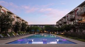Austin apartment for rent - An apartment complex with a pool and lounge chairs at dusk.